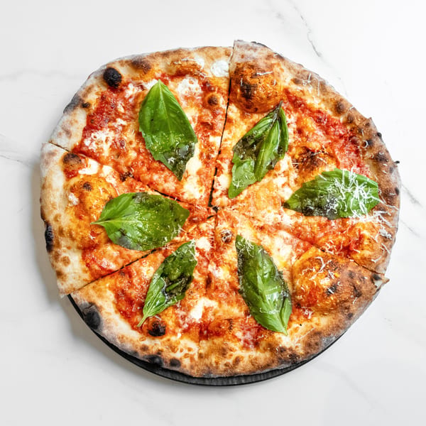 A sliced Margherita pizza with fresh basil leaves and grated cheese on a white marble surface.