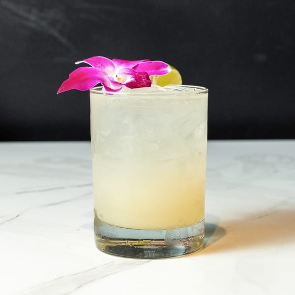 A refreshing cocktail with ice, garnished with a vibrant pink orchid and a lime wedge.