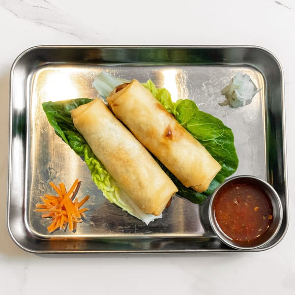 Two crispy spring rolls on lettuce with shredded carrots, pickled onions, and dipping sauce.