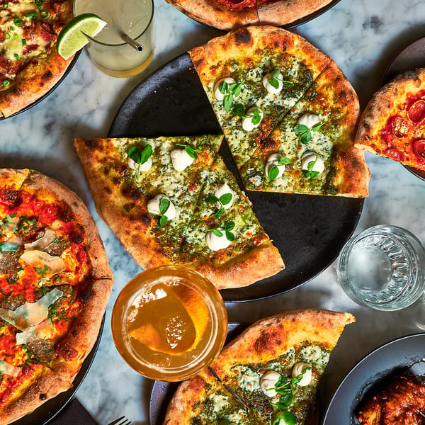 Overhead view of various pizzas, drinks, and a waffle dish on a marble table.