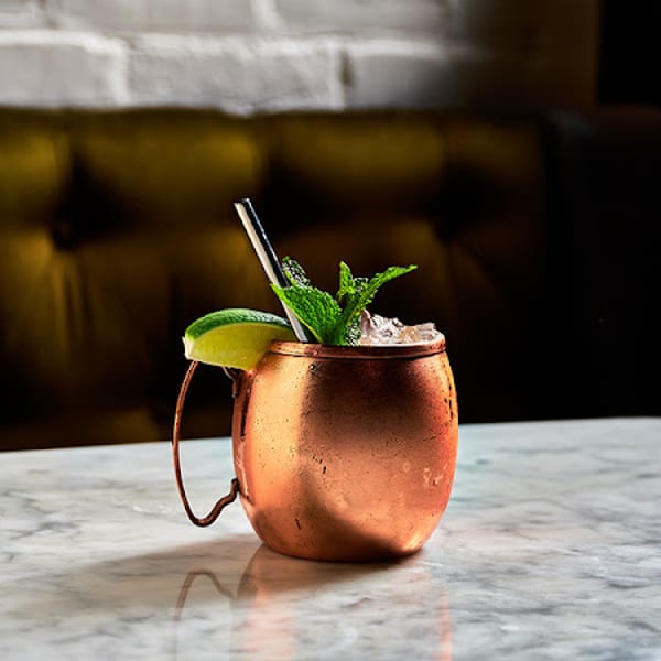 A copper mug cocktail with lime and mint on a marble table, with a brick wall background.