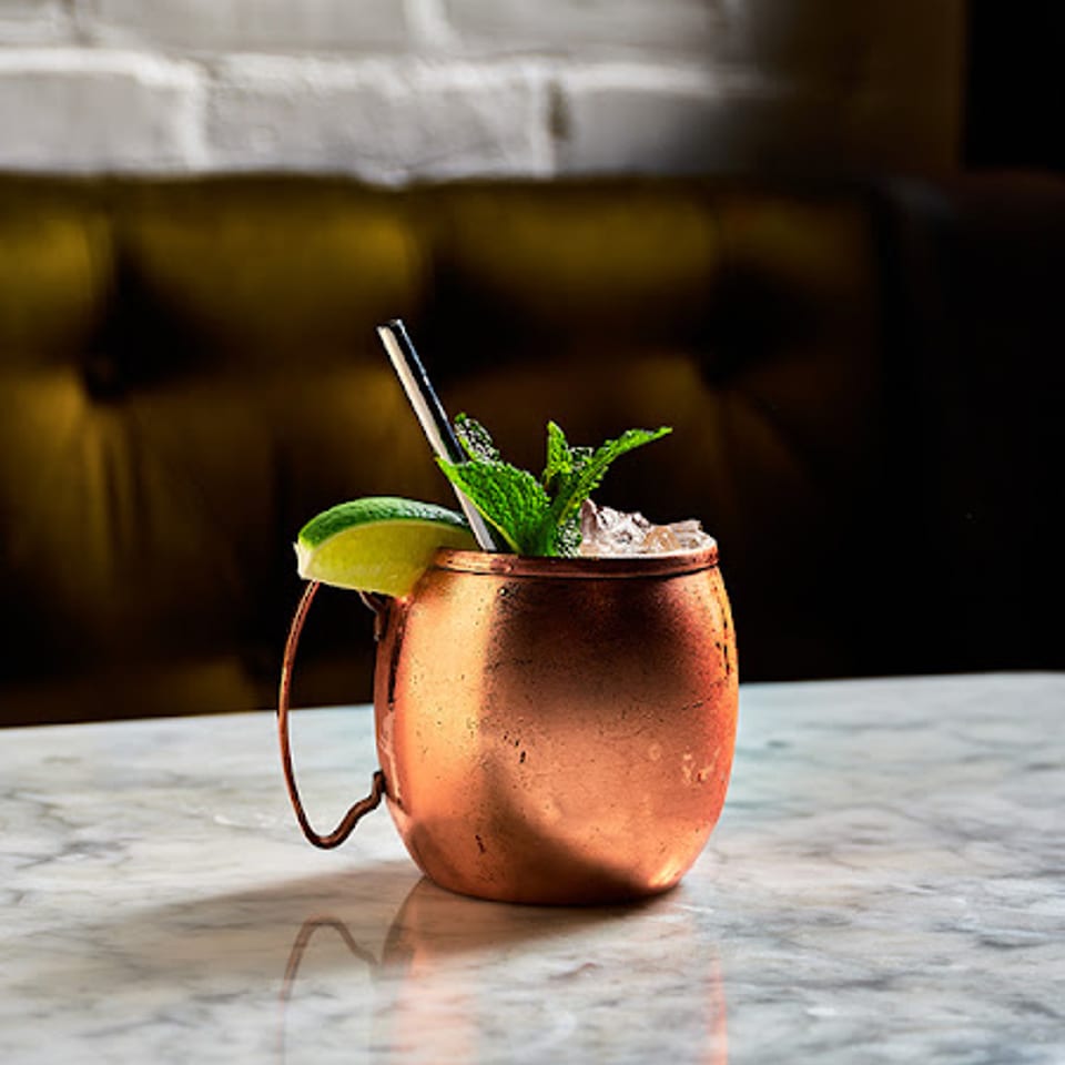 A copper mug cocktail with lime and mint on a marble table, with a brick wall background.