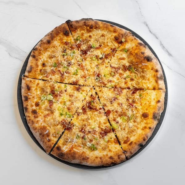 A whole, sliced pizza with bacon, cheese, and green onions on a black plate.
