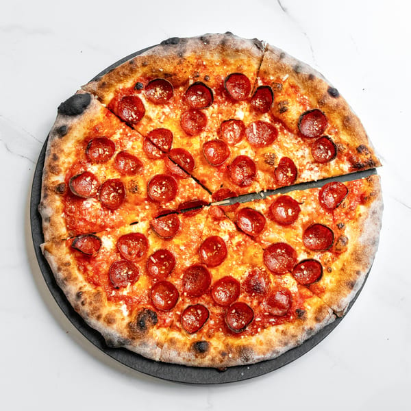 A whole pepperoni pizza, sliced into eight pieces, on a black plate against a white marble background.
